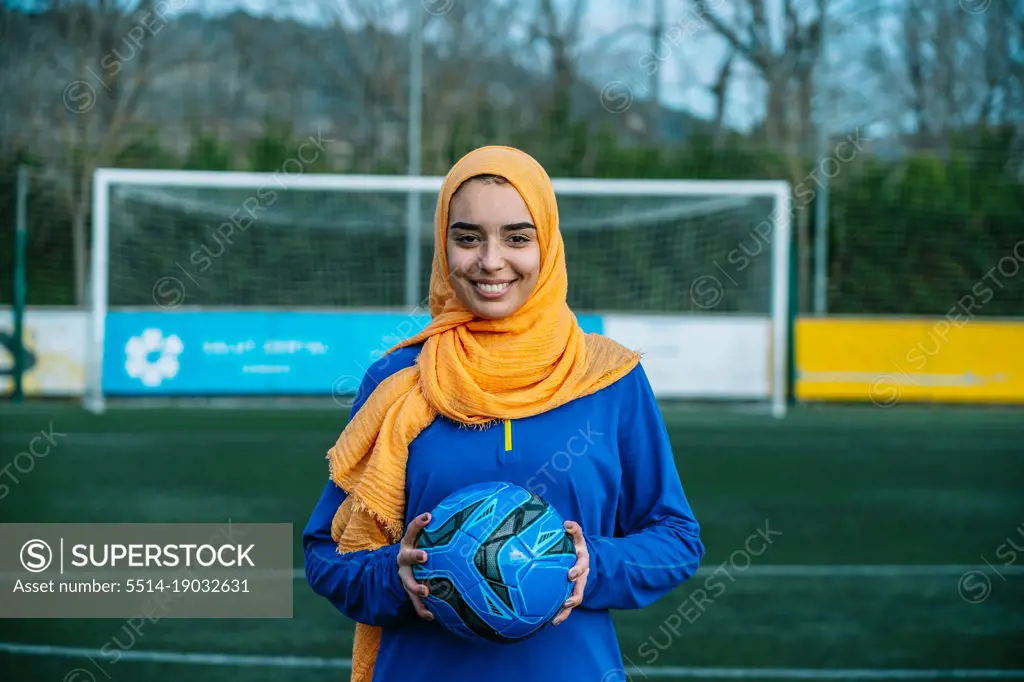 Smiling Arab female with ball on football field