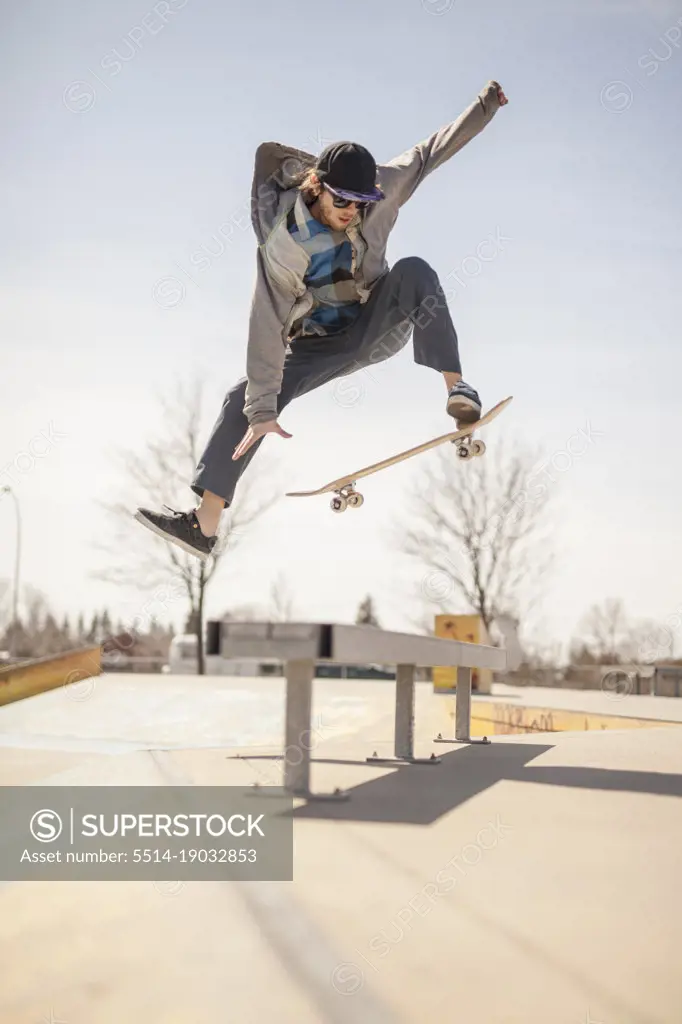 Young skateboard enthusiast in skatepark jumping over bench