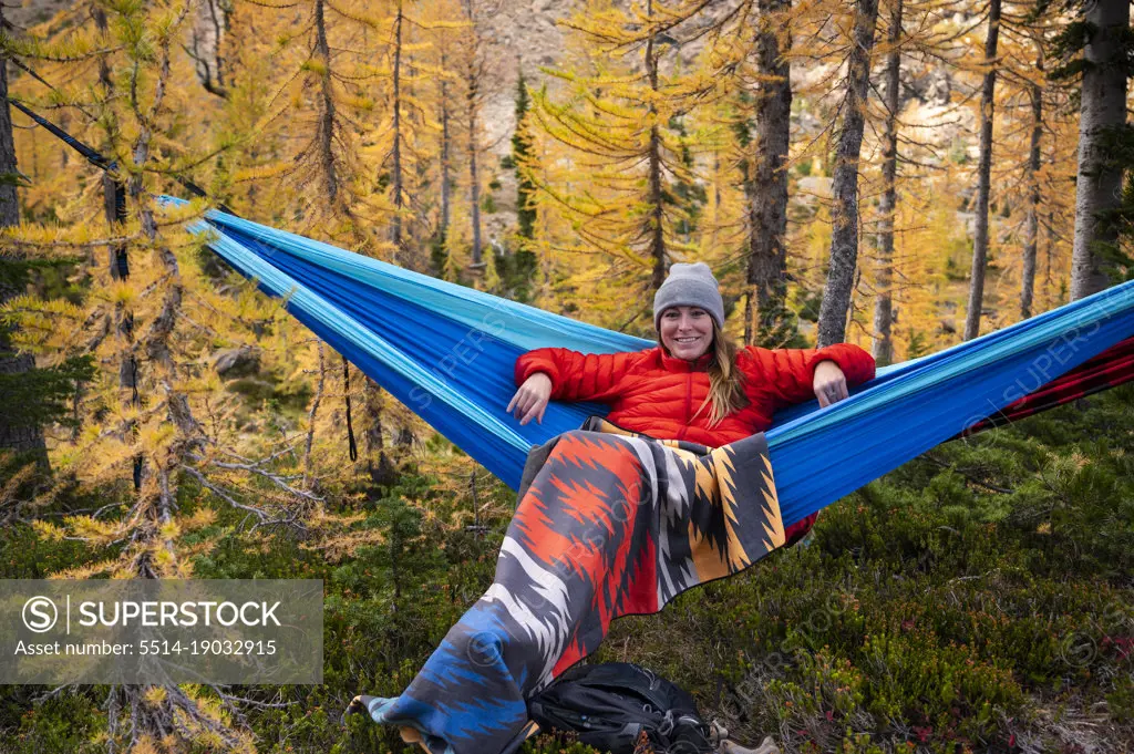 Female relaxing in a hammock in a forest of larches during autumn