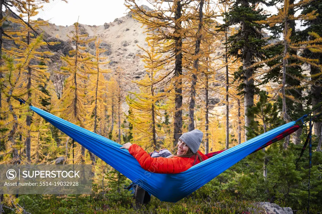 Female smiling in a hammock in a forest of larches during autumn