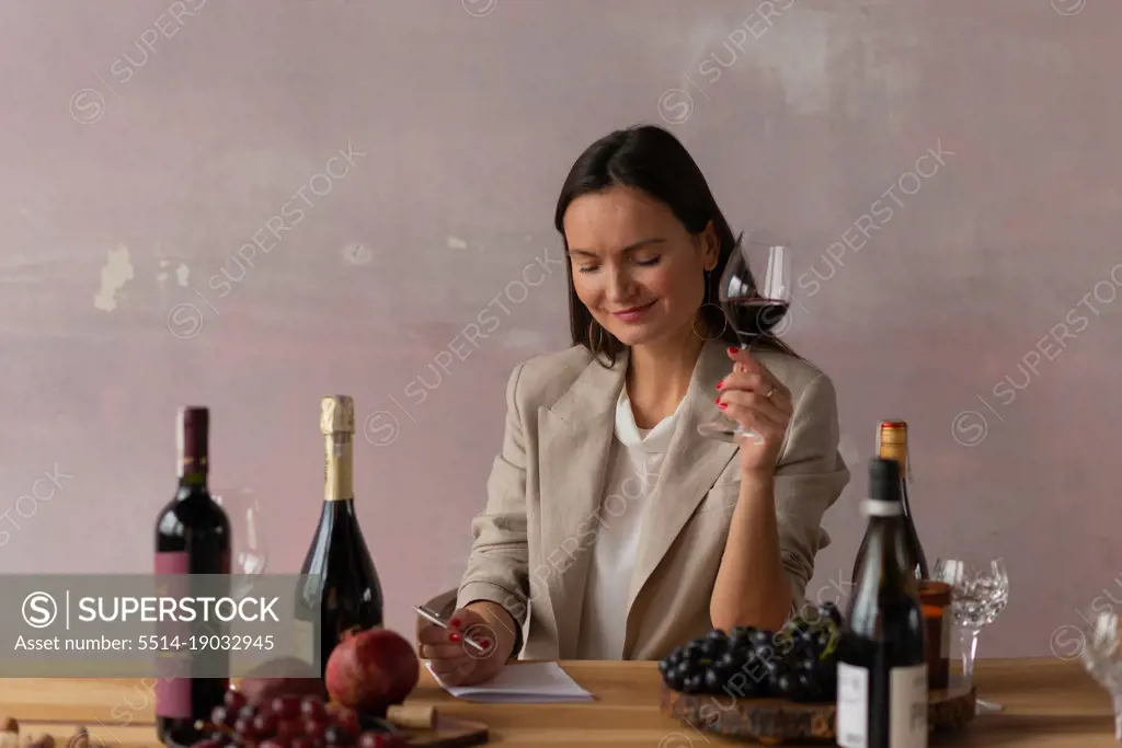 Sommelier woman doing degustation of wine, writing notes and smiling