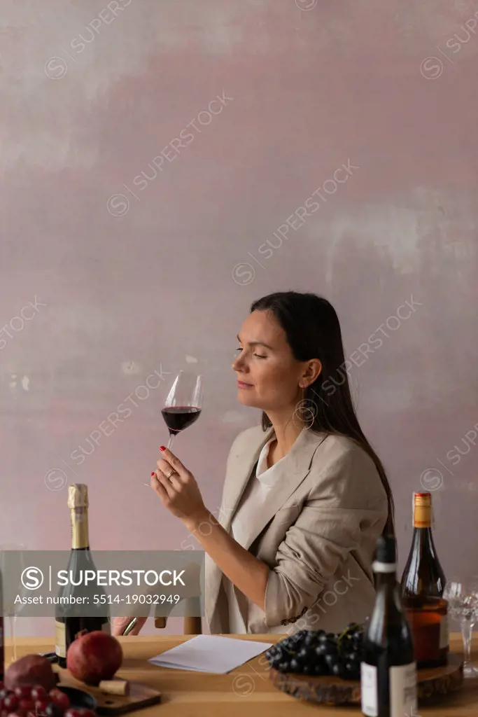 Beautiful female sommelier on degustation of wine on pink background