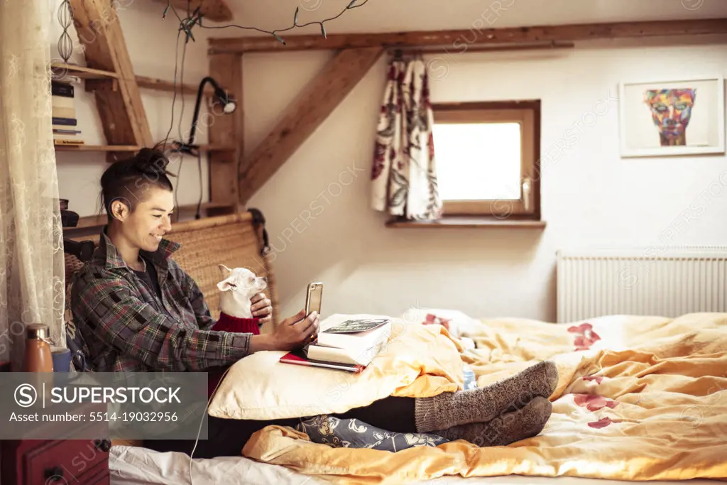 Mixed race woman sits on bed with dog and video chat's on phone