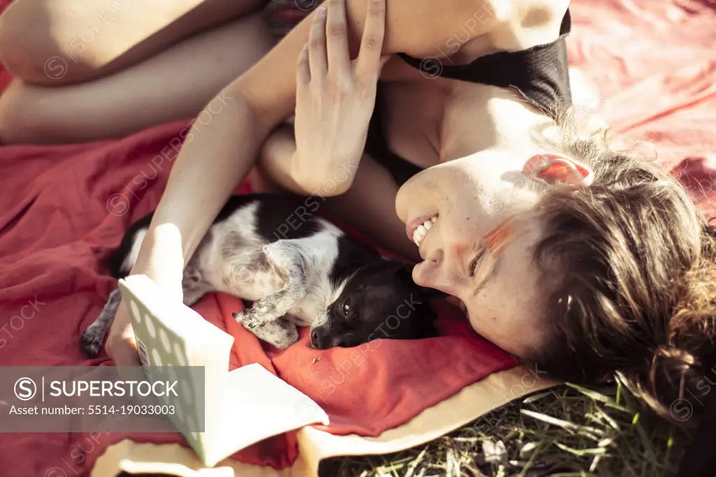 Beautiful woman smiles and reads to tiny puppy on an afternoon picnic