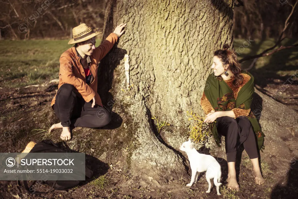 Barefoot couple smiling at the base of a large tree with small dog