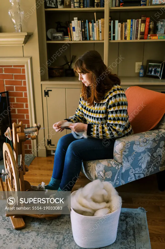 woman sitting in her living room spinning wool roving into yarn