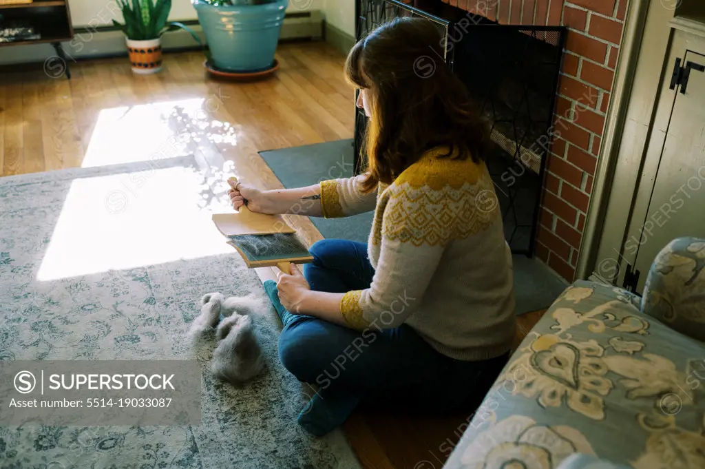 woman sitting in her living room brushing out wool roving