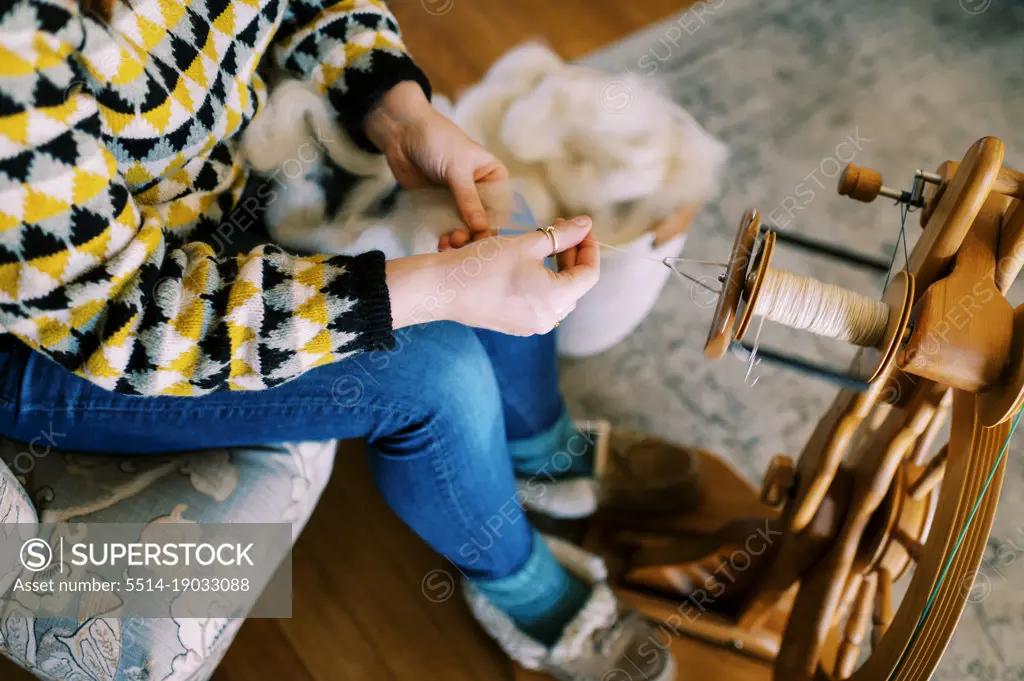 woman sitting in her living room spinning wool roving into yarn