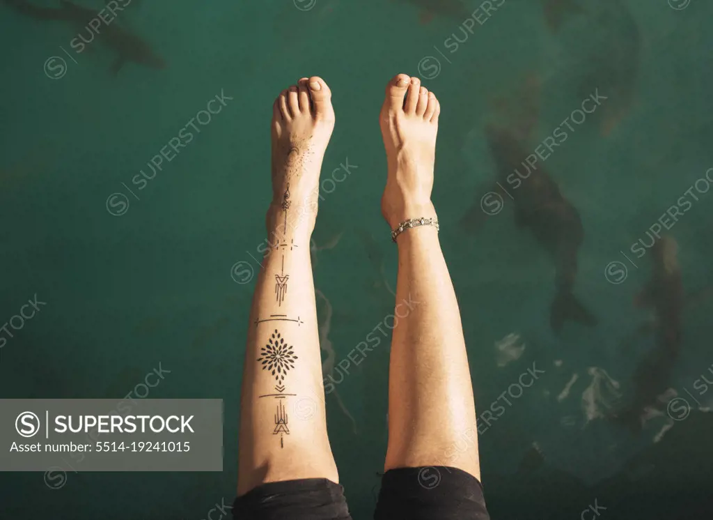 Shot of a girl's legs with tattoos and water in the background.