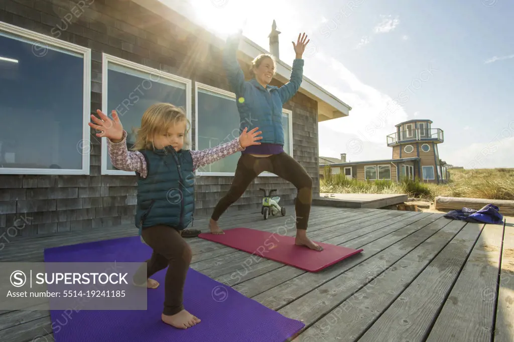 A young girl and her mother do yoga on a sunny deck