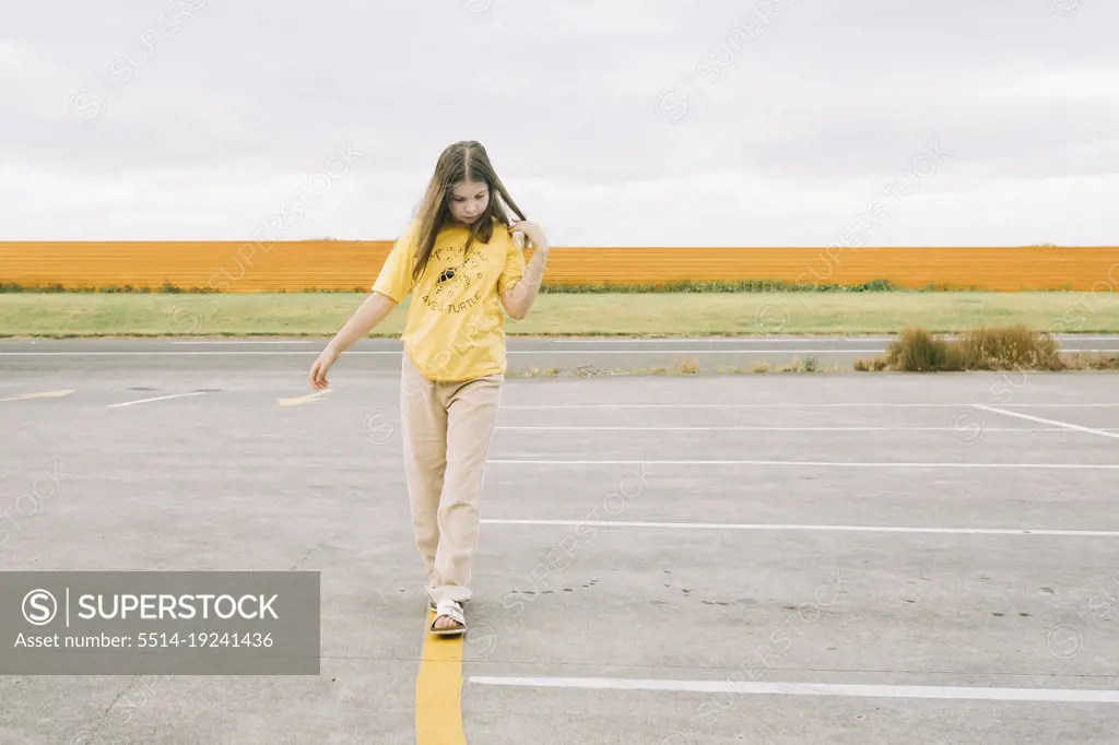 Young girl walking along painted yellow line in car park