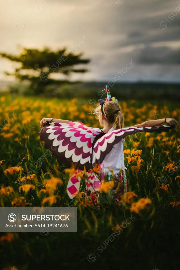 Blond girl child with butterfly wings in orange flower field playing