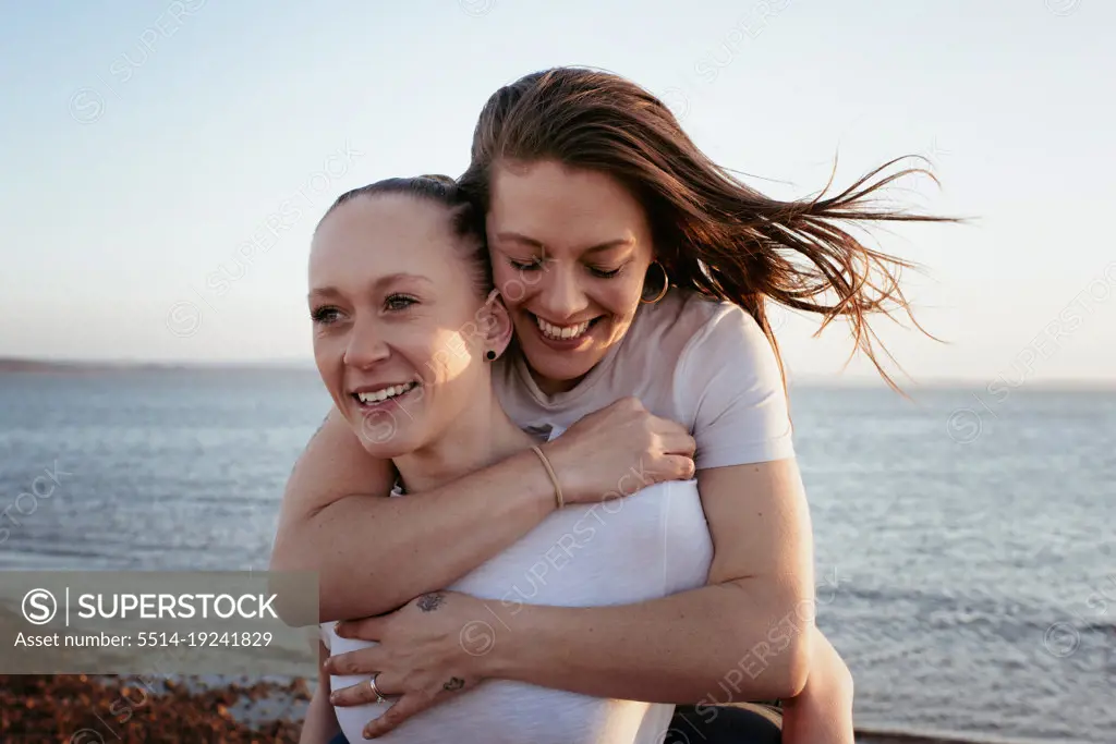 lesbian couple carrying each other at the beach happily at sunset