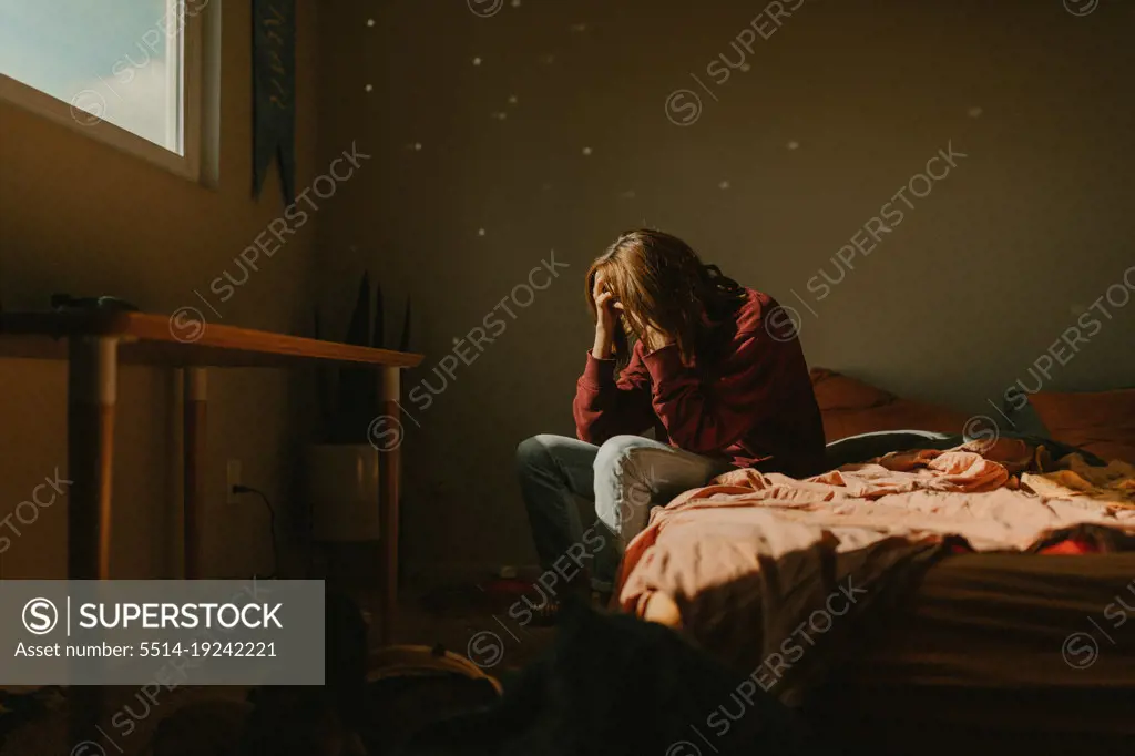 a woman with head in hands feeling anxiety and depression by window