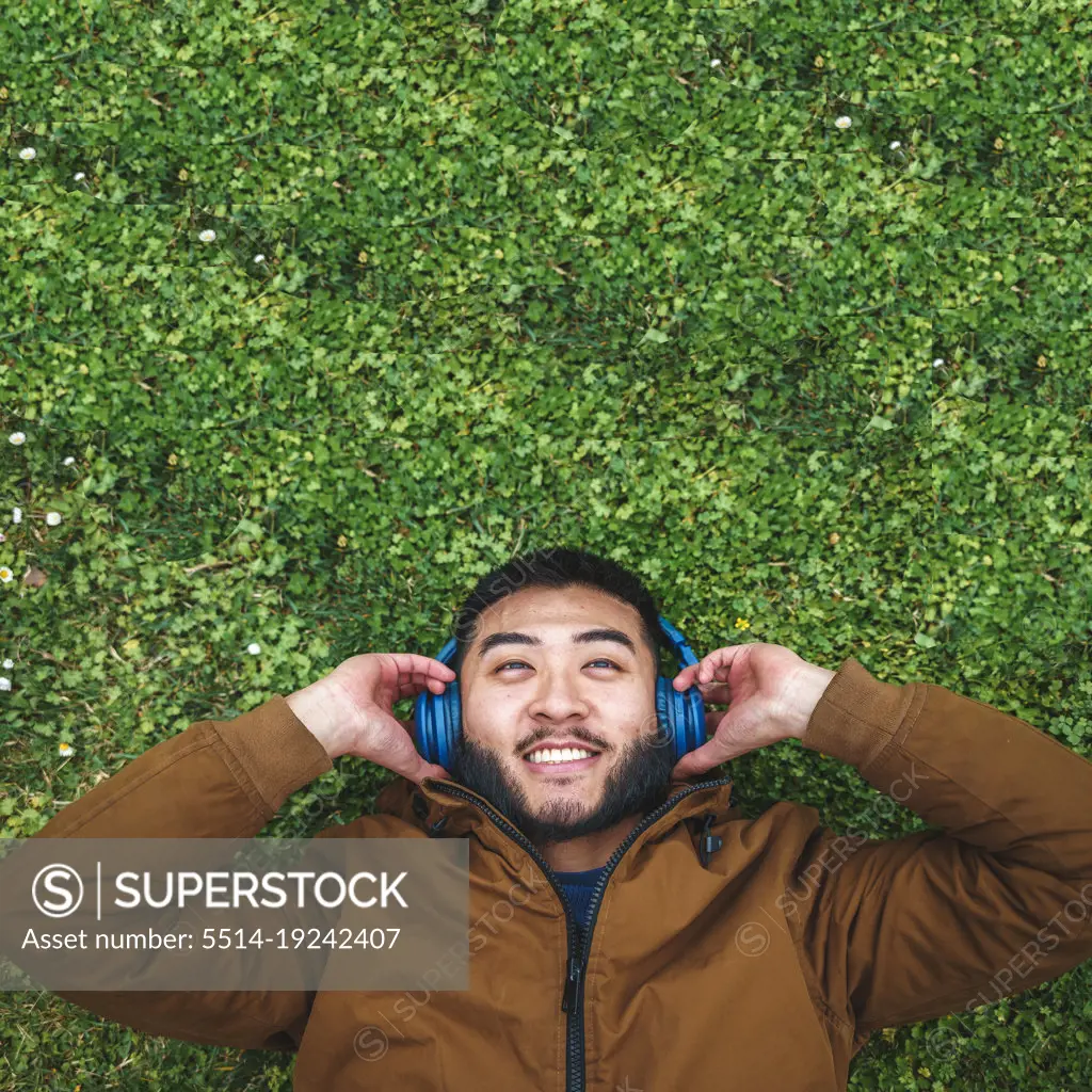 Happy ethnic man enjoying music in headphones on grass