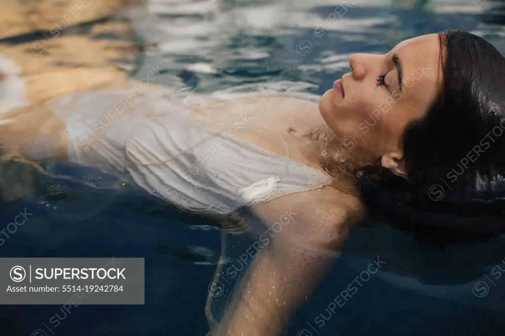 Wet young girl emerging head from water wearing white swimsuit - SuperStock
