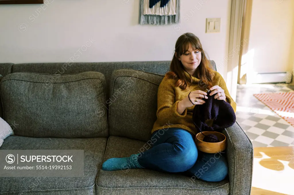 Relaxed woman sitting on couch and knitting a sweater