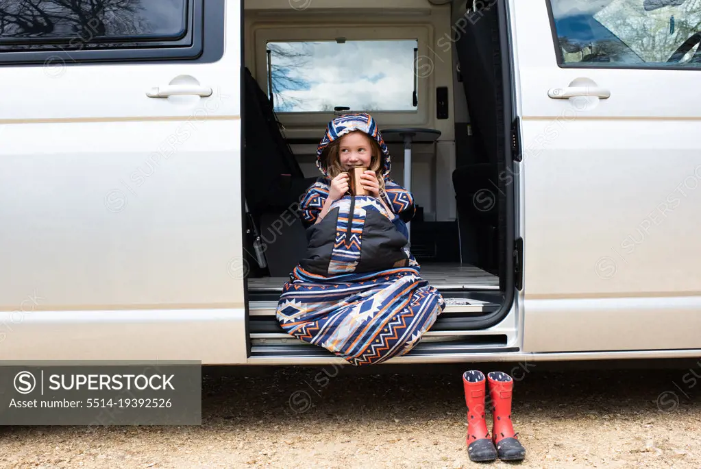 child enjoying a hot chocolate in the doorway of a campervan