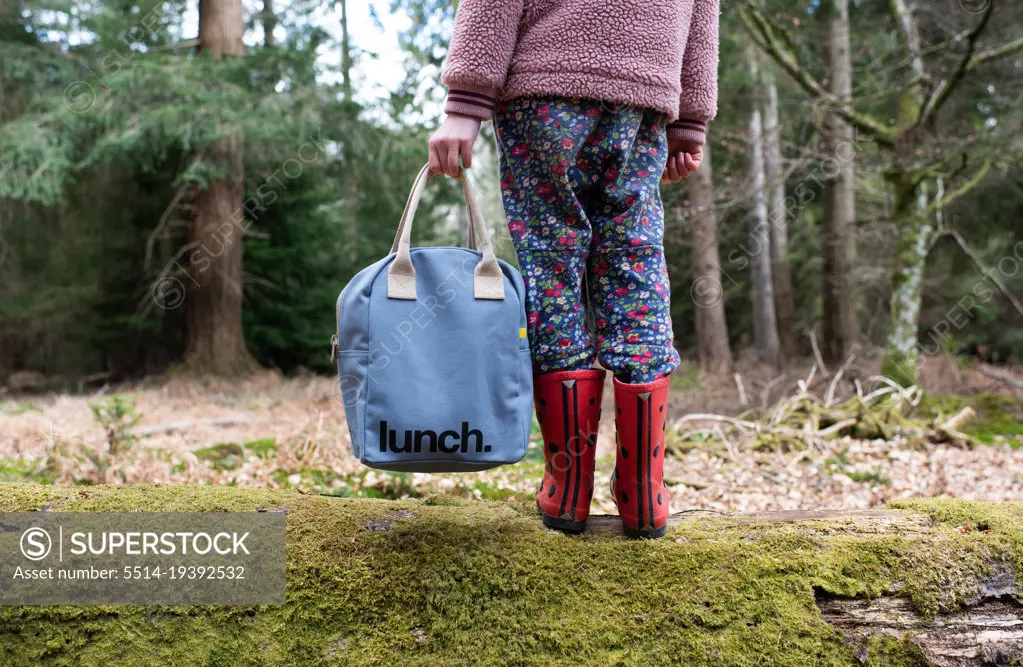 child holding onto a picnic lunch bag whilst walking in the forest