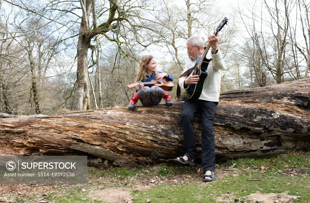 grandfather playing guitar with his granddaughter in the forest