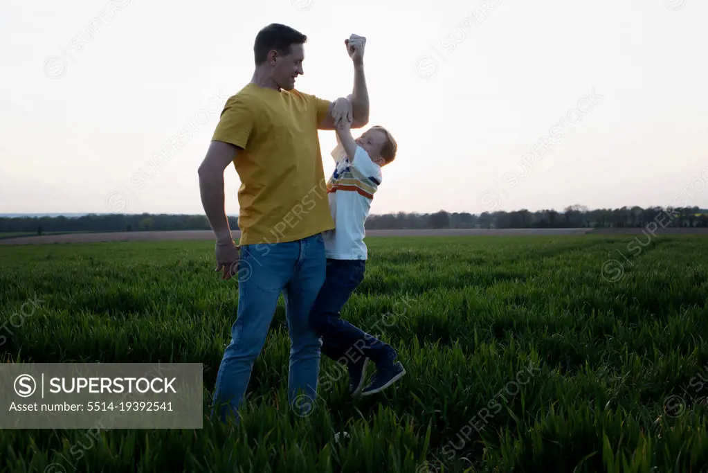 father flexing his muscles whilst son hangs on his arm playfully
