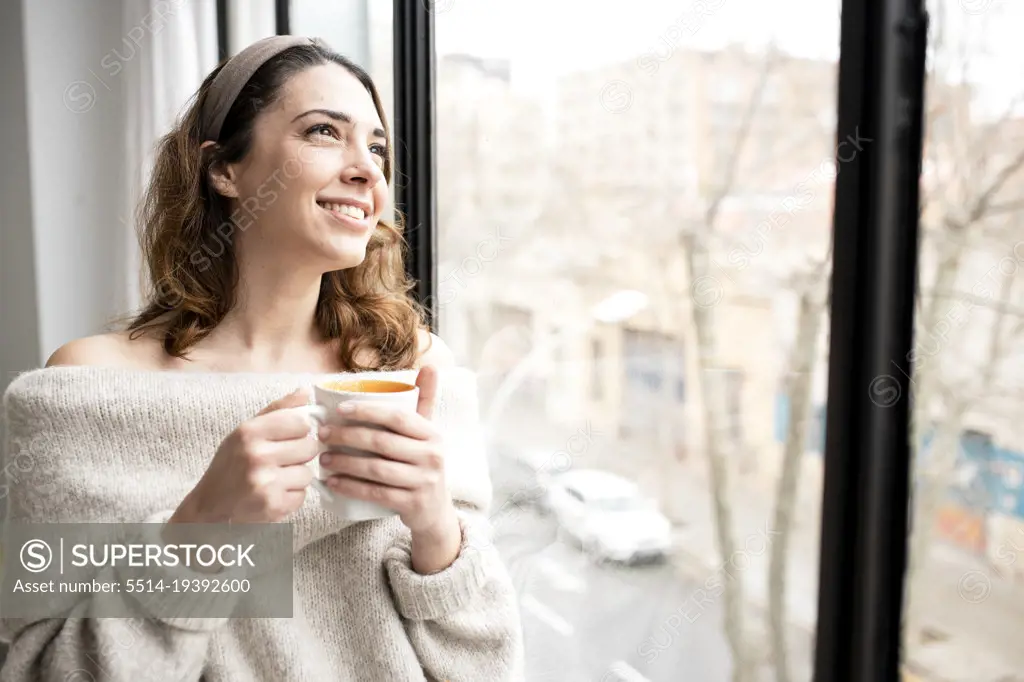 Young female having morning tea and looking out of window