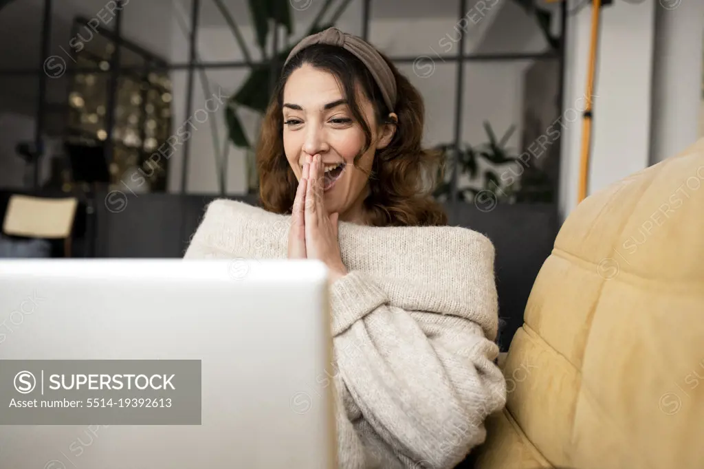 Excited woman looking at laptop screen sitting on cozy sofa at home