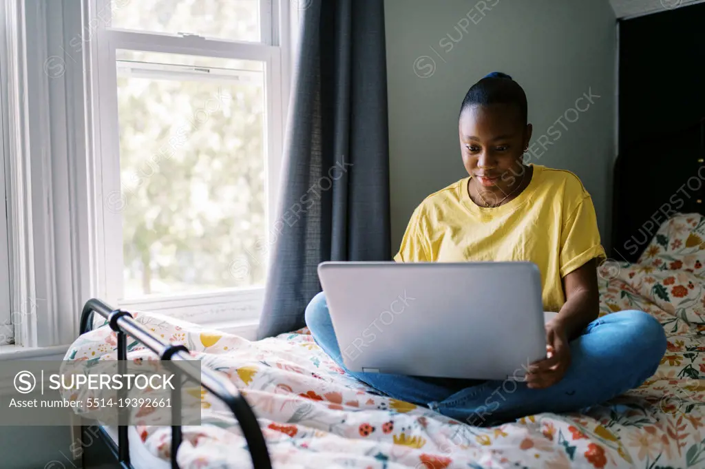 young laughing black teen sitting on bed with computer