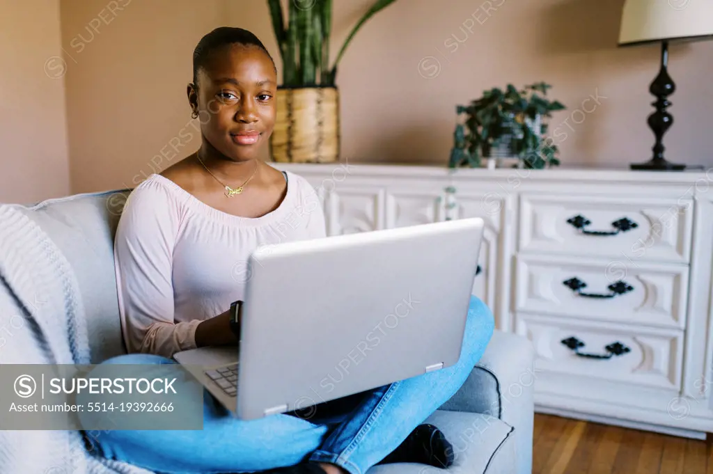 Teenage girl sitting on couch with laptop on her lap