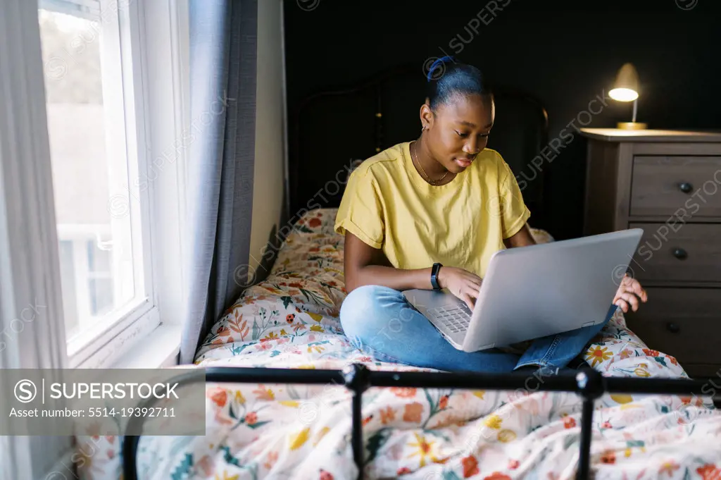 Happy teenage girl sitting on bed with her computer