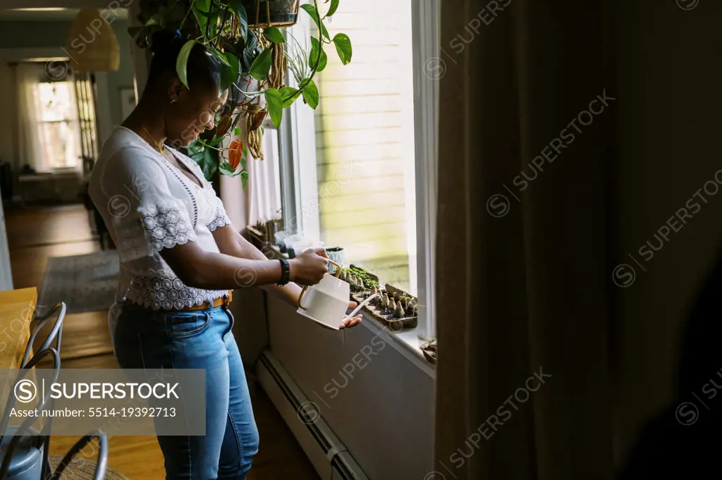 young teenage girl watering her seedlings on her window sill