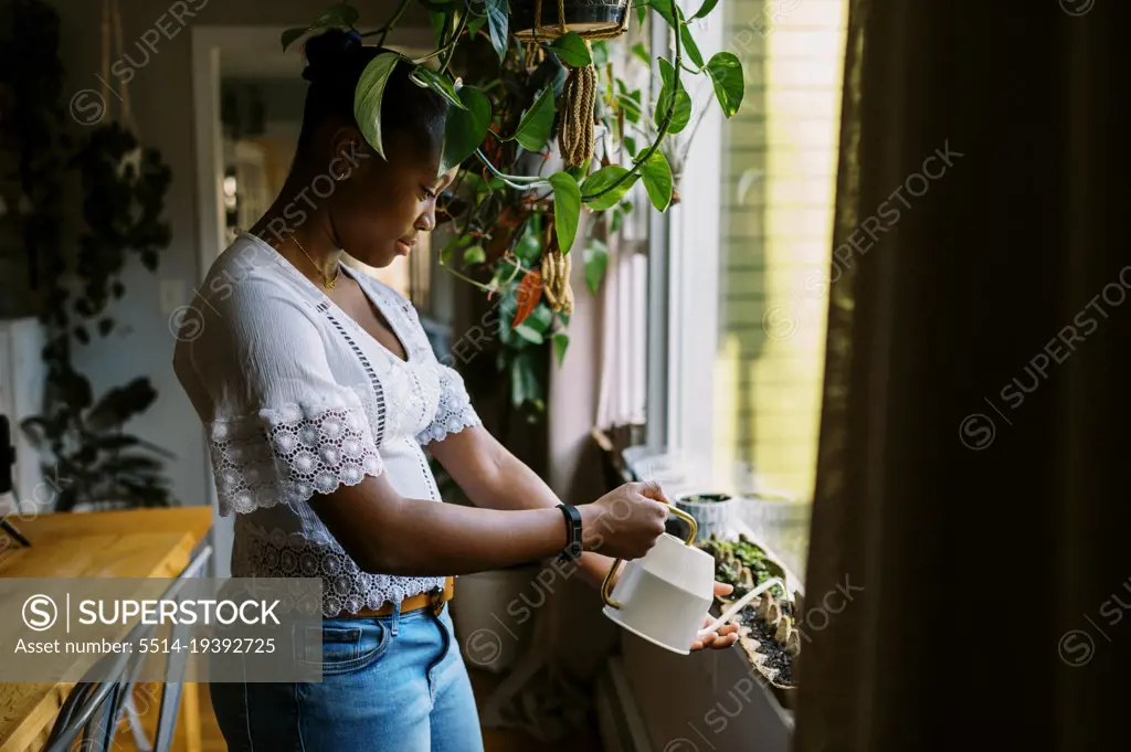Young black teenage girl watering her plants on the window sill