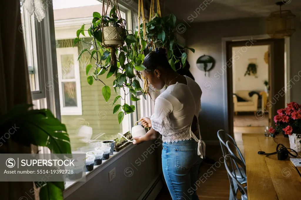 Young black teenage girl watering her seedlings on the window sill