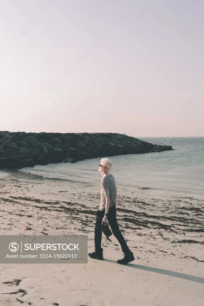 Albino man walking on the beach holding a hat