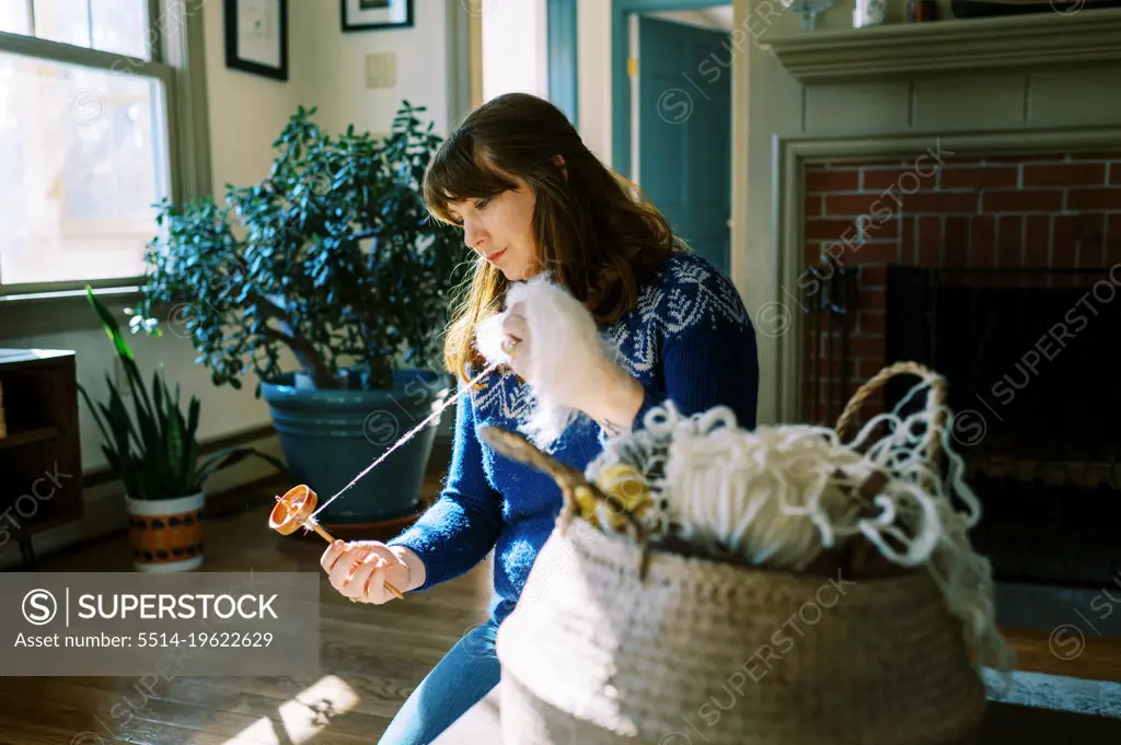 woman sitting on floor making yarn with her drop spindle
