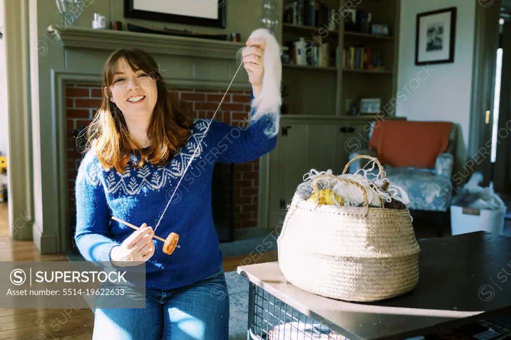 smiling woman working with her drop spindle in living room