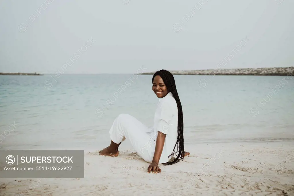 Woman with braids sitting at the beach wearing white outfit