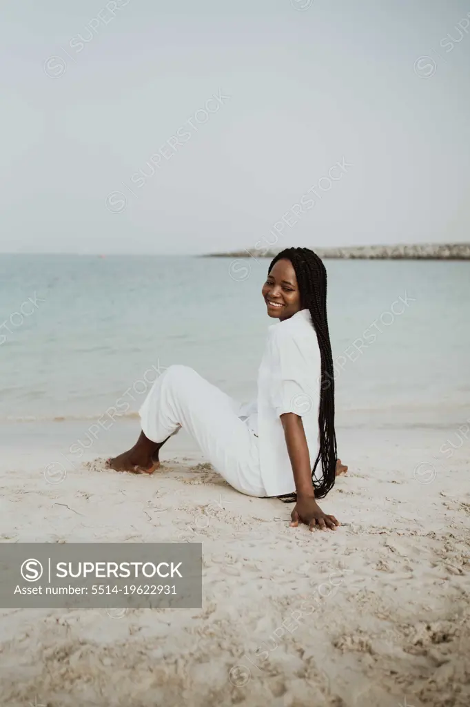 Woman with braids sitting at the beach wearing white outfit