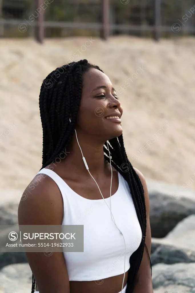 Woman with braids sitting at the beach wearing headphones