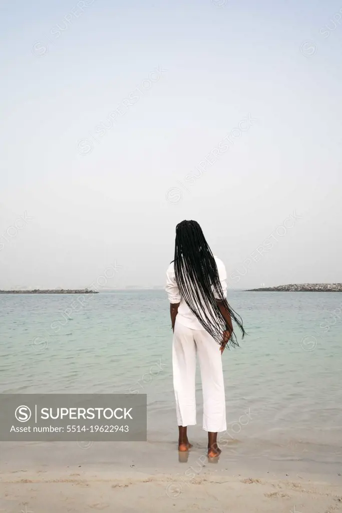 View from behind on woman with braids standing at the beach 