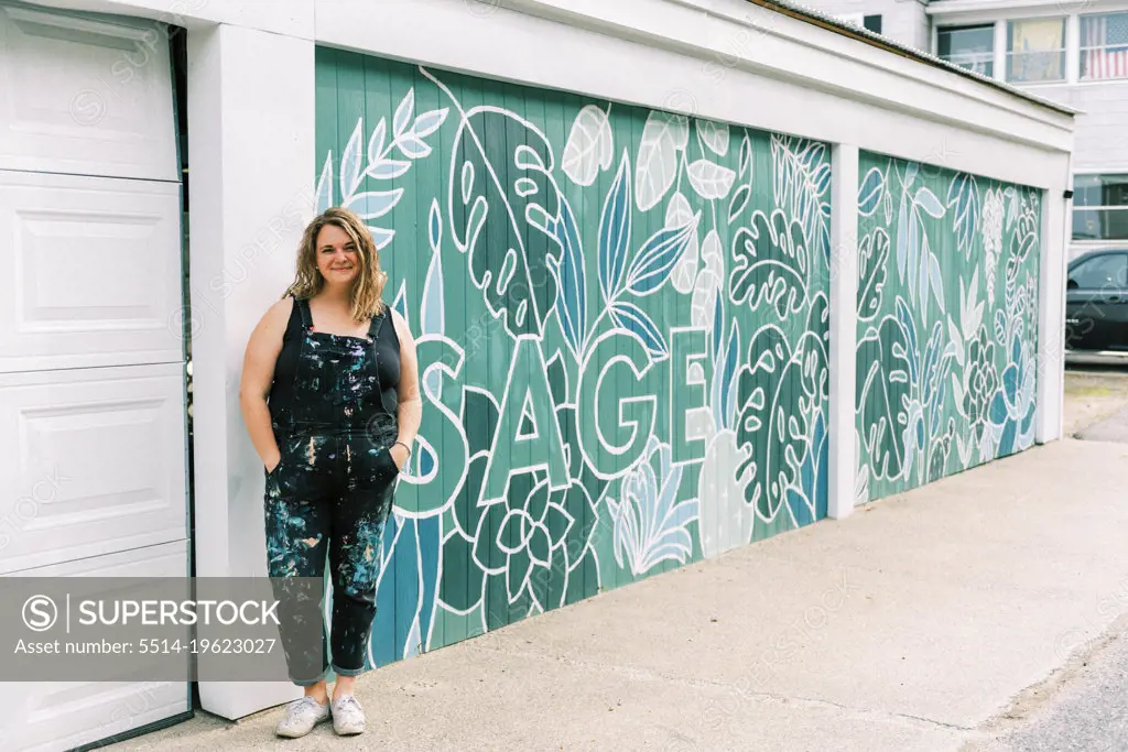 female artist standing next to hear painted mural