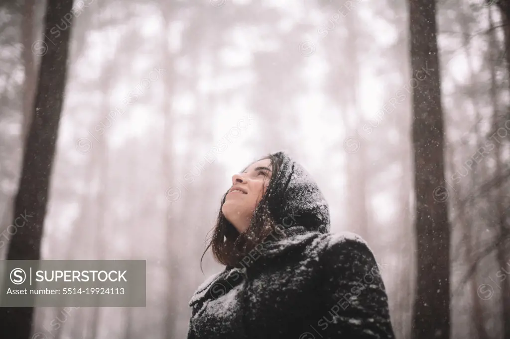 Portrait of happy young woman standing in forest during snowfall
