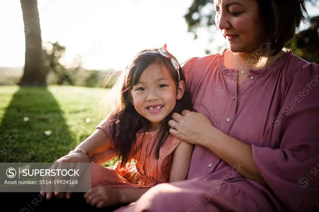 Asian Girl Smiles for Camera, Sitting with Mom in Park in San Diego