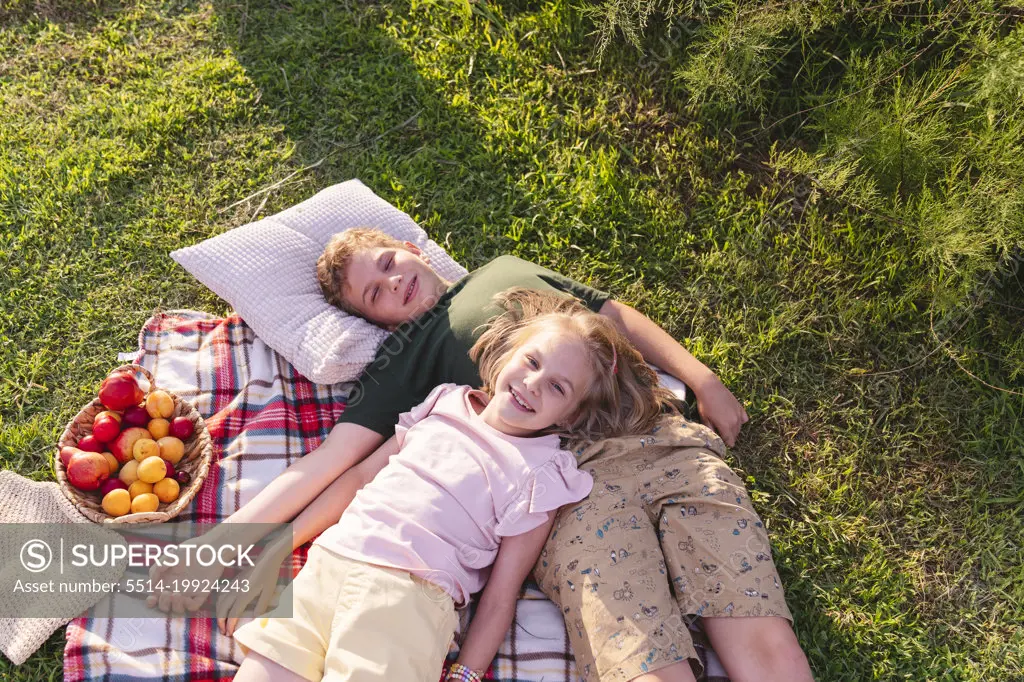 Brother and sister on a picnic resting on a picnic blanket.