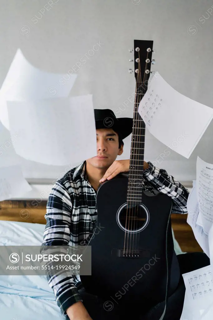 Latin man with  guitar on bed with note sheets floating around