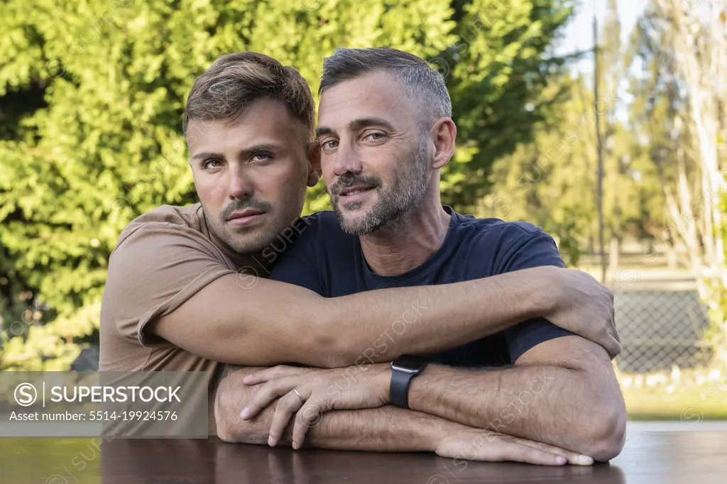 A young man hugging his husband outdoors.  Both are looking at camera