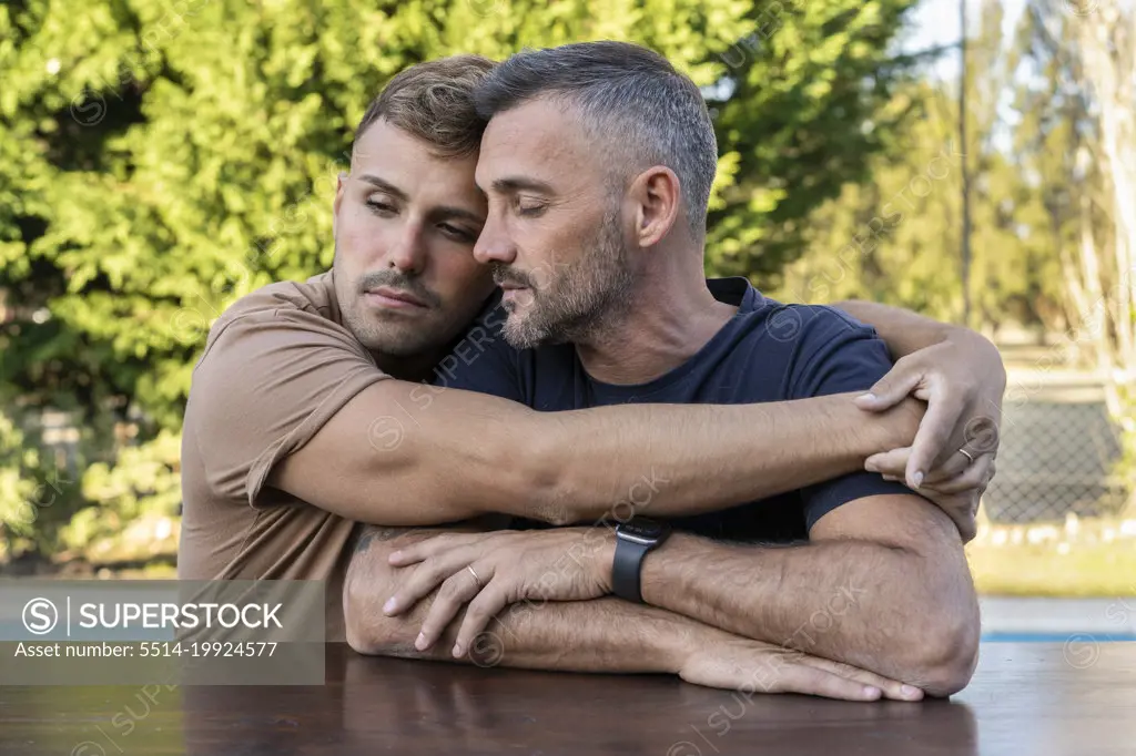 A young man hugging his husband outdoors.  Both with eyes closed