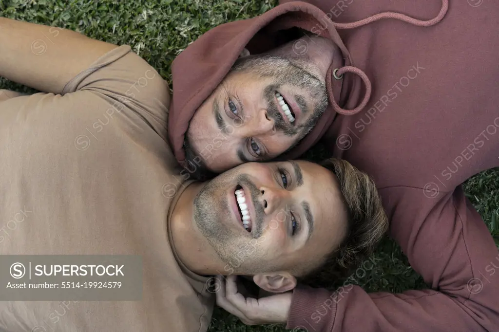 Top view of a male gay couple lying on the grass, looking at camera