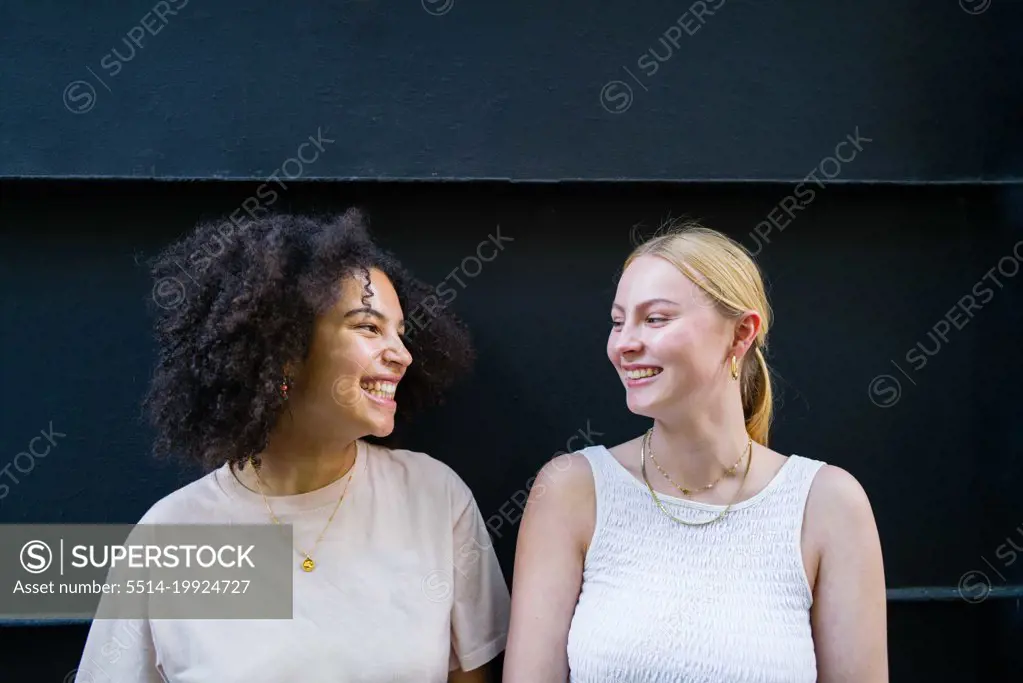 Portrait of two young diverse female looking at each other smiling