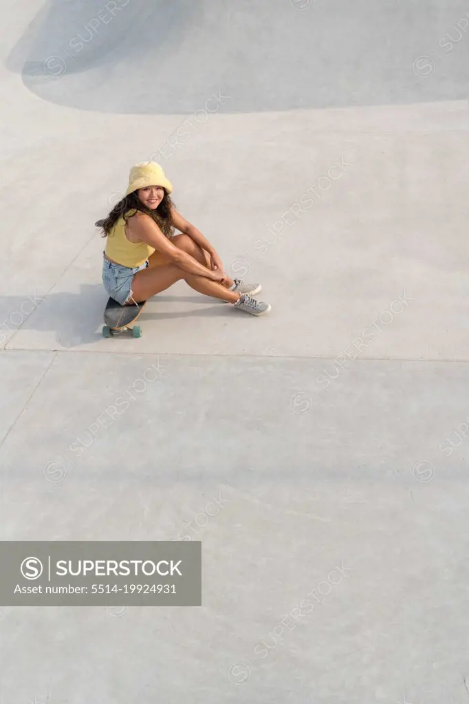Asian woman sitting on her skateboard in the skate park